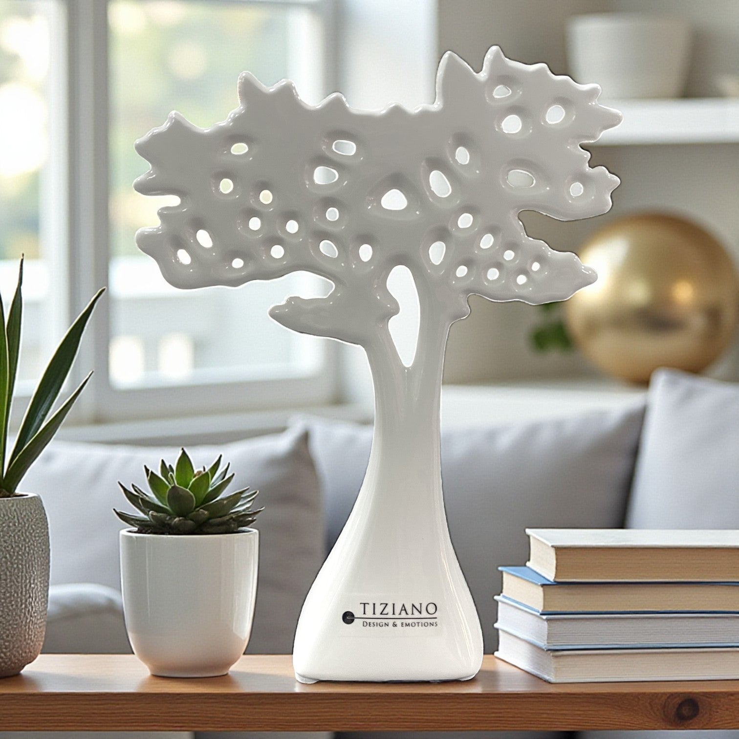 Ein weißer Keramikbaum mit durchbrochener, strukturierter Baumkrone steht als Dekoelement auf einem Tisch neben einem Sukkulententopf und Büchern.