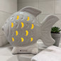 Ein weißer Keramik-Fisch mit integrierter LED-Beleuchtung leuchtet warm durch die ausgestanzten Muster und steht auf einer Badezimmerablage.