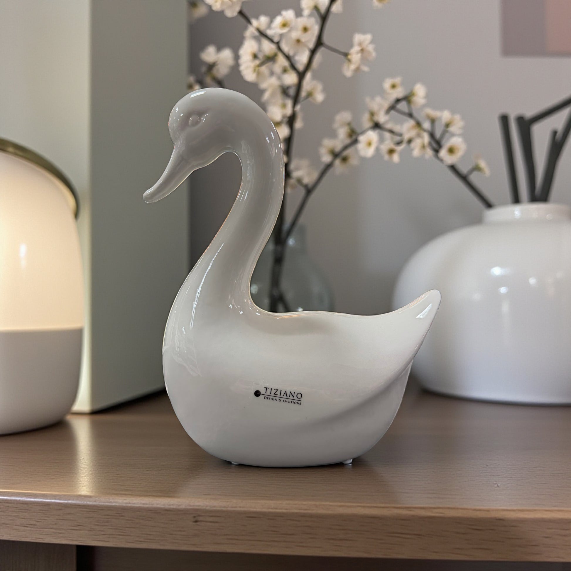 Große weiße Keramikfigur in Gansform steht dekorativ auf einem Möbelstück neben einer Lampe und Vasen.