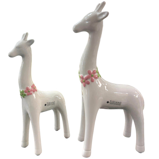 Zwei weiße Keramik-Giraffen mit rosa Blumenkränzen stehen freigestellt vor weißem Hintergrund nebeneinander.