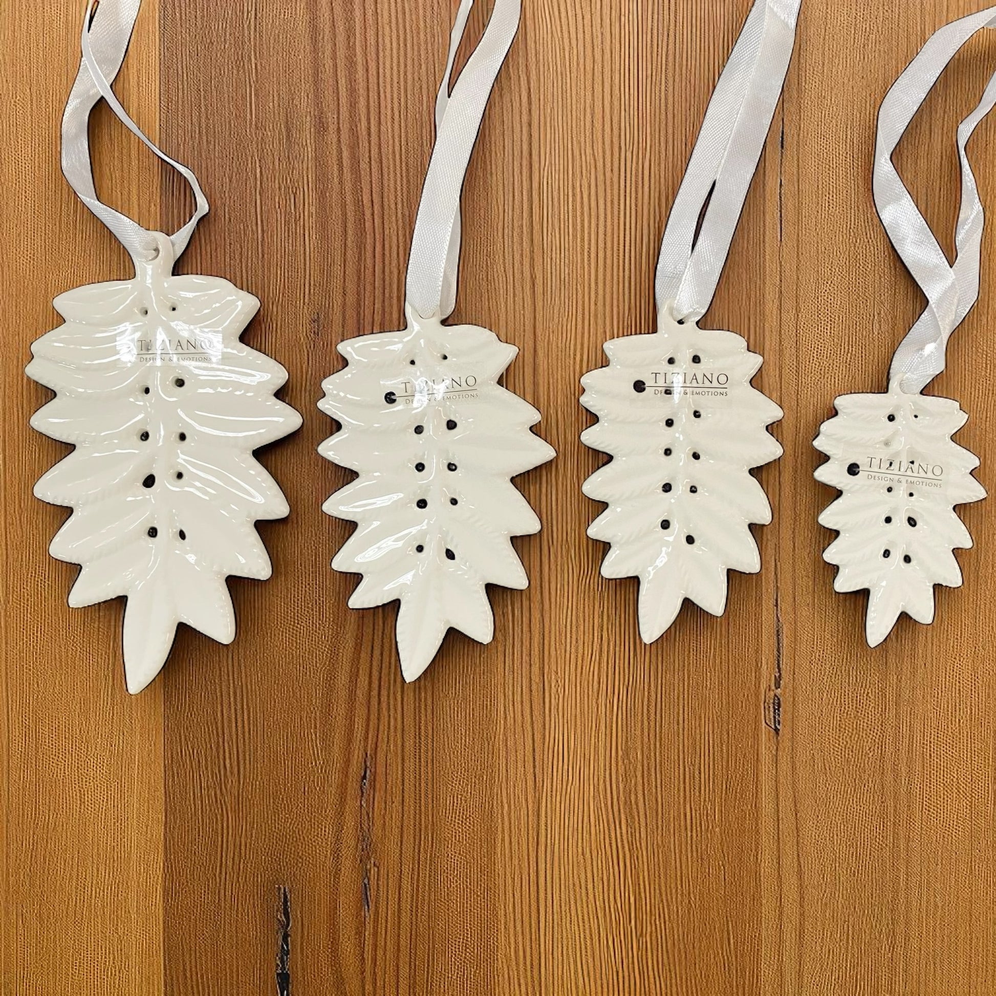 Unterschiedlich große Blatt-Anhänger aus Keramik in glänzendem Weiß, jeweils mit Tiziano Logo und Satinband zum Aufhängen im Ambiente