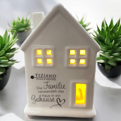 Ein Tiziano Lichterhaus aus creme-weißer Keramik mit LED Beleuchtung & Spruch "die Familie verwandelt das Haus in ein Zuhause" im Ambiente