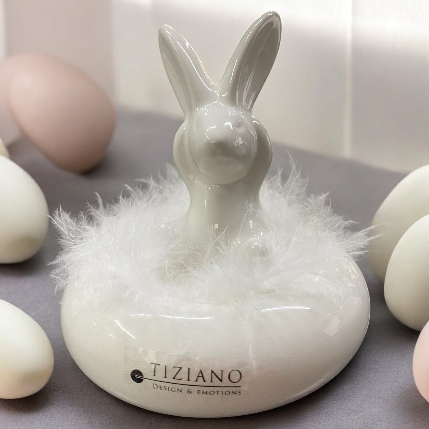 Tiziano Deko Osterhase Fabrio stehend auf Keramiksockel aus creme-weißer Keramik mit flauschigem Federschmuck im Ambiente.