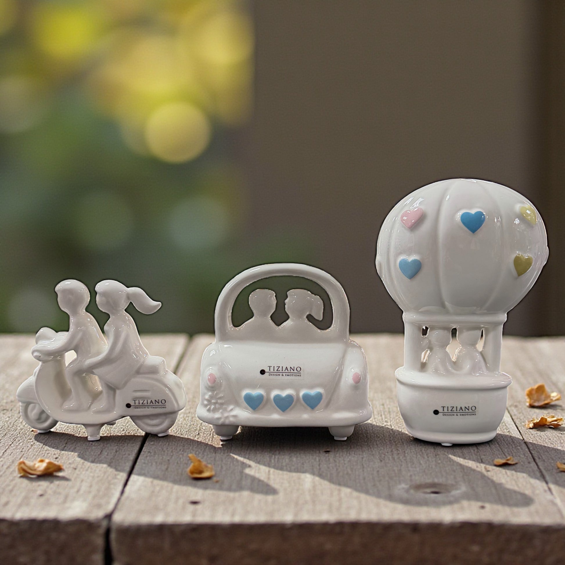 Drei weiße Keramik Dekofiguren mit Paarmotiven auf Holzoberfläche dekorativ nebeneinander arrangiert.