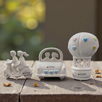 Drei weiße Keramik Dekofiguren mit Paarmotiven auf Holzoberfläche dekorativ nebeneinander arrangiert.