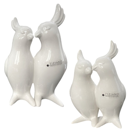 Zwei crème-weiße Keramikfiguren in Form eines Papageienpaars, eng beieinanderstehend mit liebevollem Ausdruck, in zwei Größen nebeneinander dargestellt.