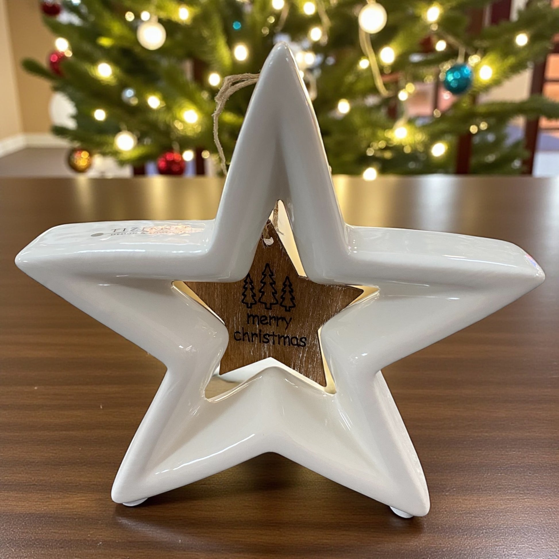Ein kleiner stehender creme-weißer Tiziano Keramik Stern Cascata mit hängendem Holzstern Merry Christmas im Ambiente 