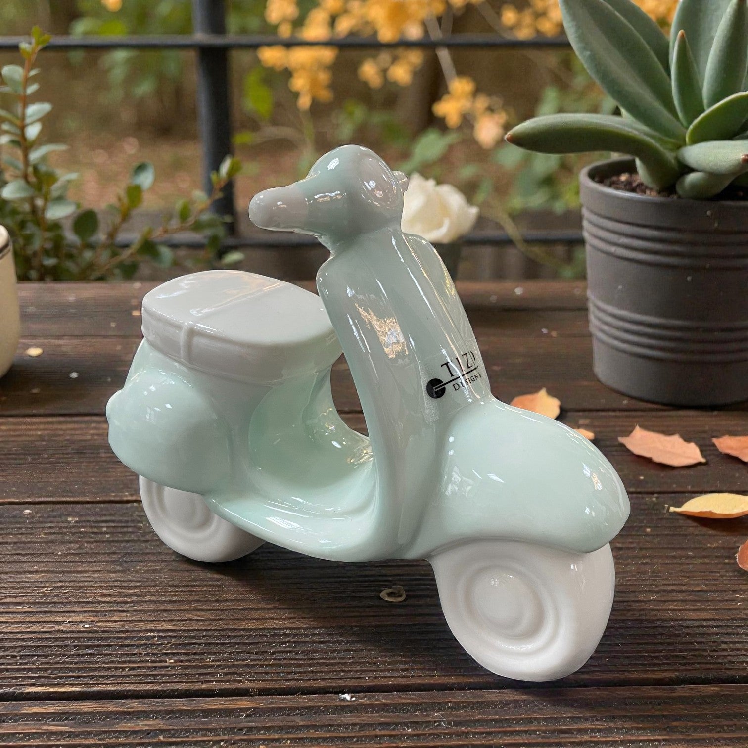 Keramik-Dekoroller in Mintgrün, stehend auf einem Holztisch im Außenbereich, mit Pflanzen im Hintergrund.