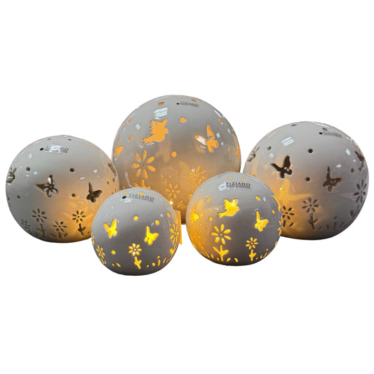 Mehrere creme-weiße Keramik-Dekokugeln mit ausgestanzten Schmetterlings- und Blumenmotiven und warm leuchtender LED-Beleuchtung, freigestellt auf weißem Hintergrund.