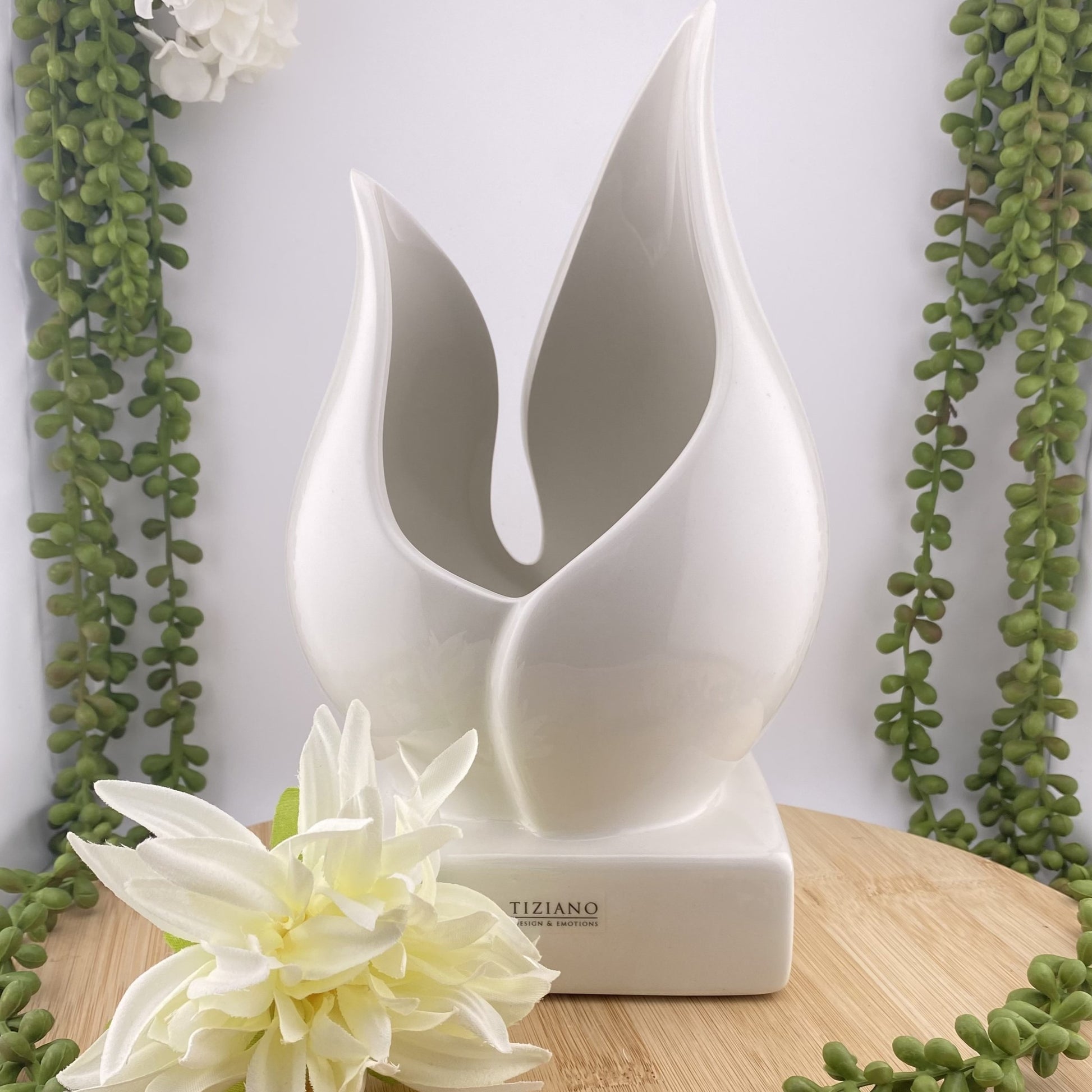 Eine Pflanzenschale aus creme-weißer Keramik ist im Ambiente platziert. Die Vase besteht aus einem Sockel, auf dem zwei Blätter eine tulpenartige Vase und damit eine Öffnung formen.