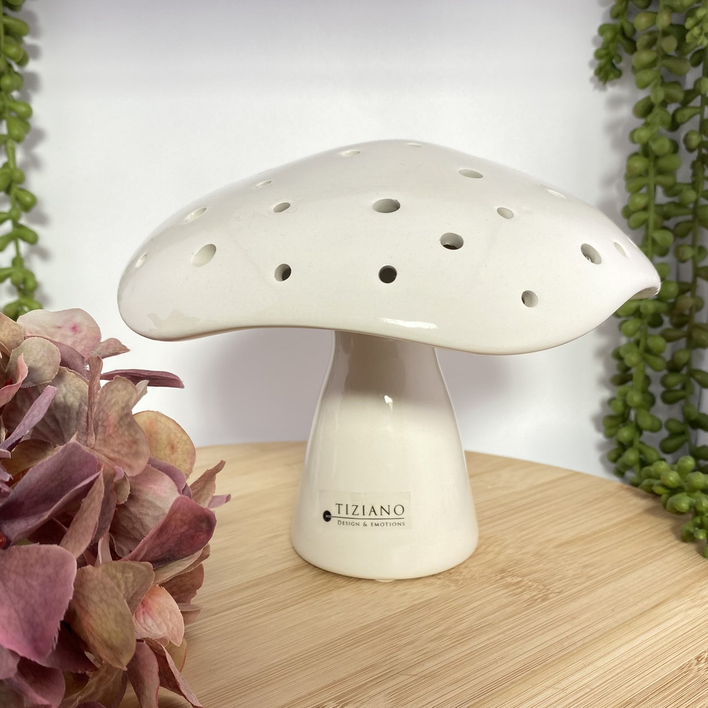 Ein großer Deko Pilz aus creme-weißer Keramik mit integrierter LED Beleuchtung und runden Aussparungen auf ihren gewölbten Hüten. Der Dekoartikel ist 20cm groß und in herbstlichem Ambiente platziert.