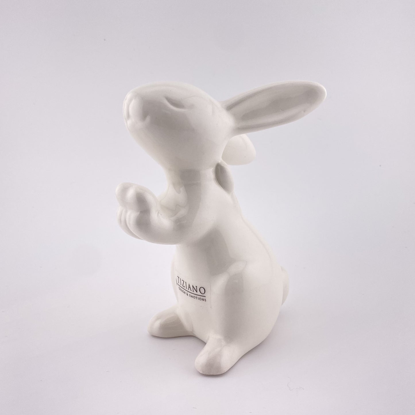 Ein 14cm großer creme-weißer Deko Keramik Hase mit großen Ohren, einer Schleife um den Hals und einem Herz in den Pfoten. Der Osterhase ist vor weißem Hintergrund platziert.