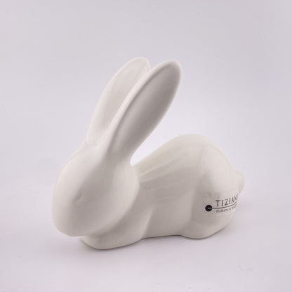 Ein schlafender Keramik Osterhase, der auf dem Boden liegt und seine Ohren ausstreckt. Der Dekohase ist aus creme-weißer Keramik gefertigt, 19cm hoch und vor weißem Hintergrund abgebildet.