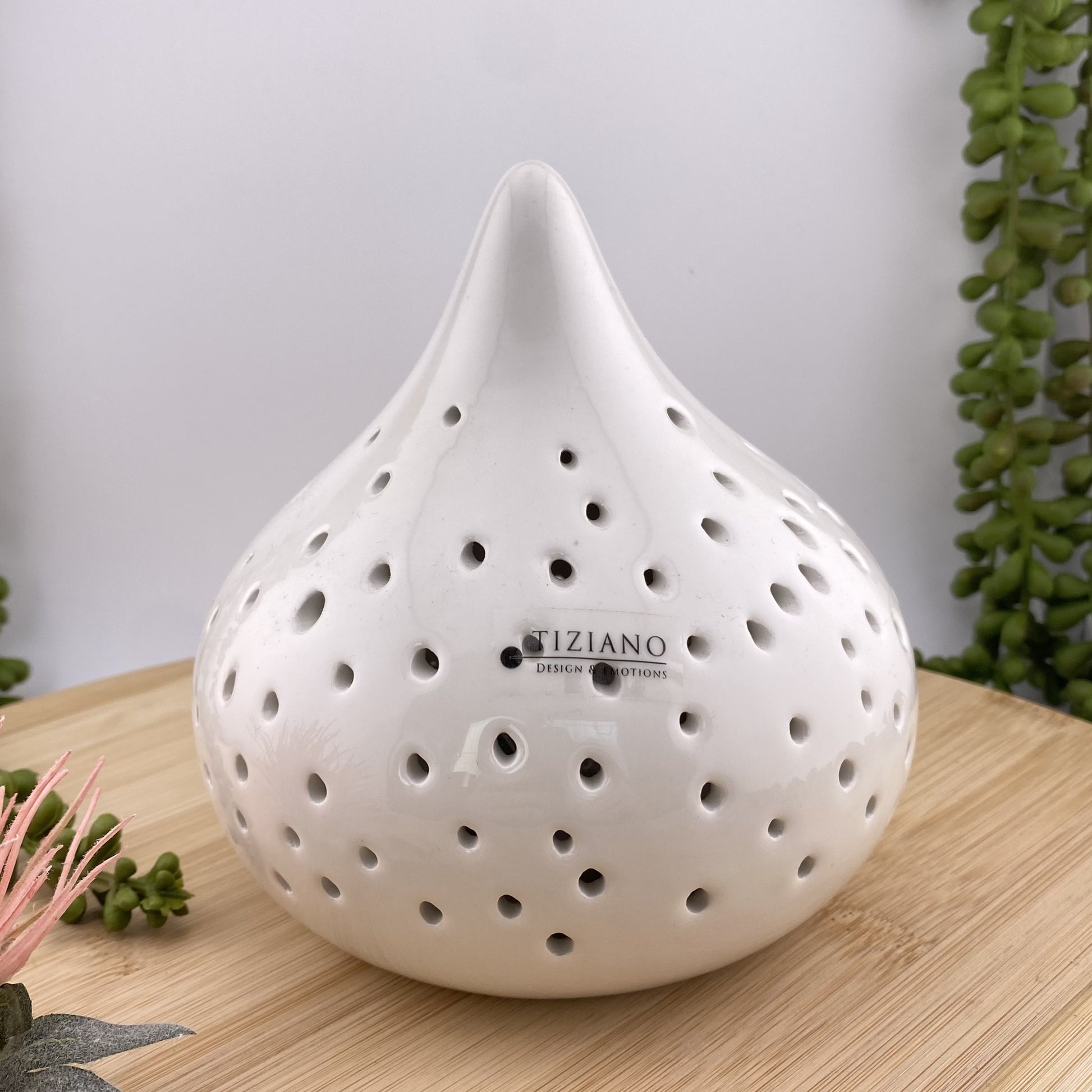 Ein großes creme-weißes Keramik Dekolicht der Serie Valeno von Tiziano, dass im Ambiente platziert ist. Im Inneren befindet sich eine LED Beleuchtung. Die Form ist tropfenförmig und auf dem Objekt sind runde Aussparungen. 13cm hoch und im Ambiente.