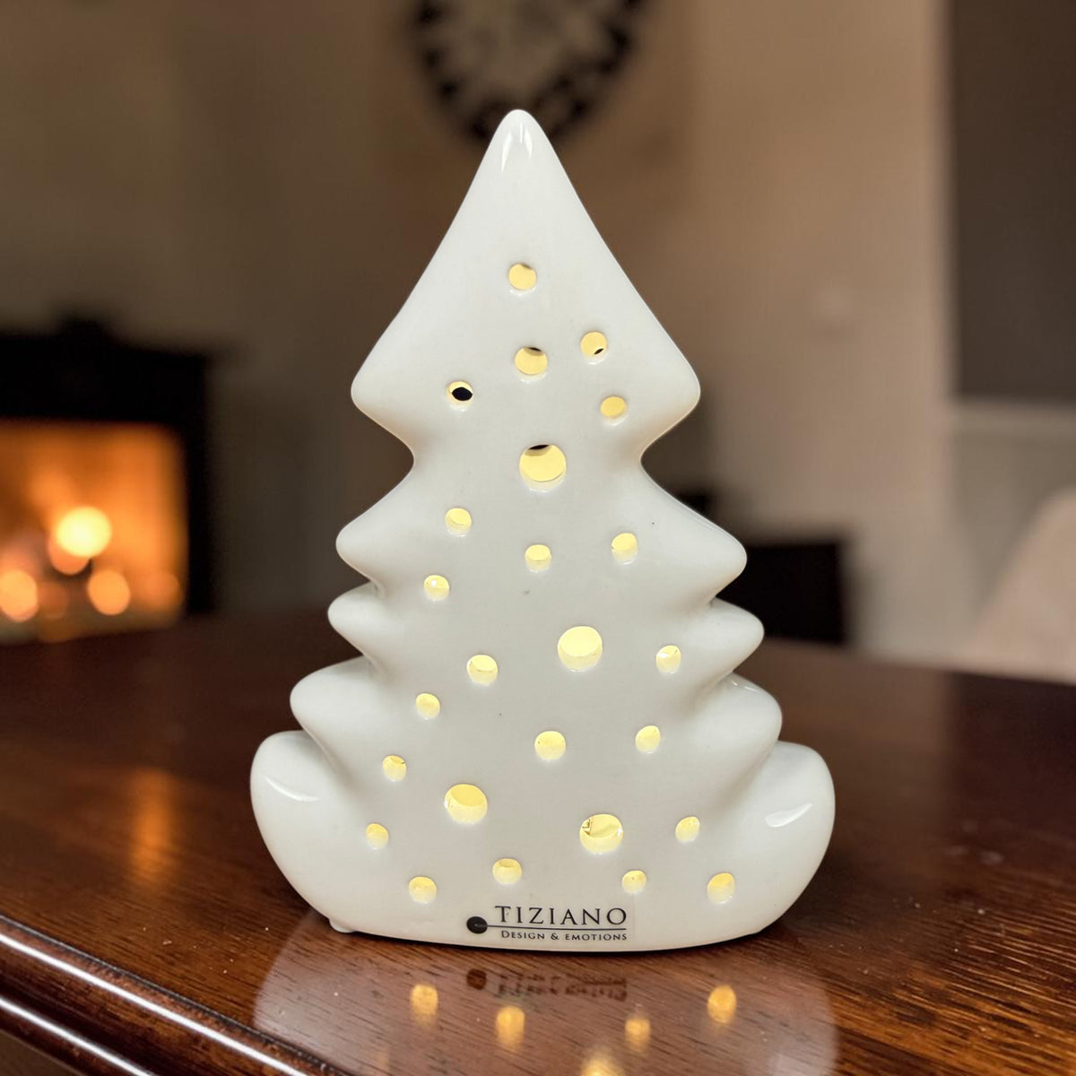 Cremeweißer Tiziano Keramik Baum Alberi mit warm beleuchtetem rundem Lochmuster auf einem Holztisch vor weihnachtlichem Hintergrund.