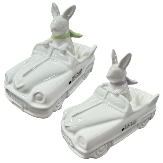 Zwei weiße Keramik Dekofiguren in Form eines Autos, in denen jeweils ein Osterhase sitzt.