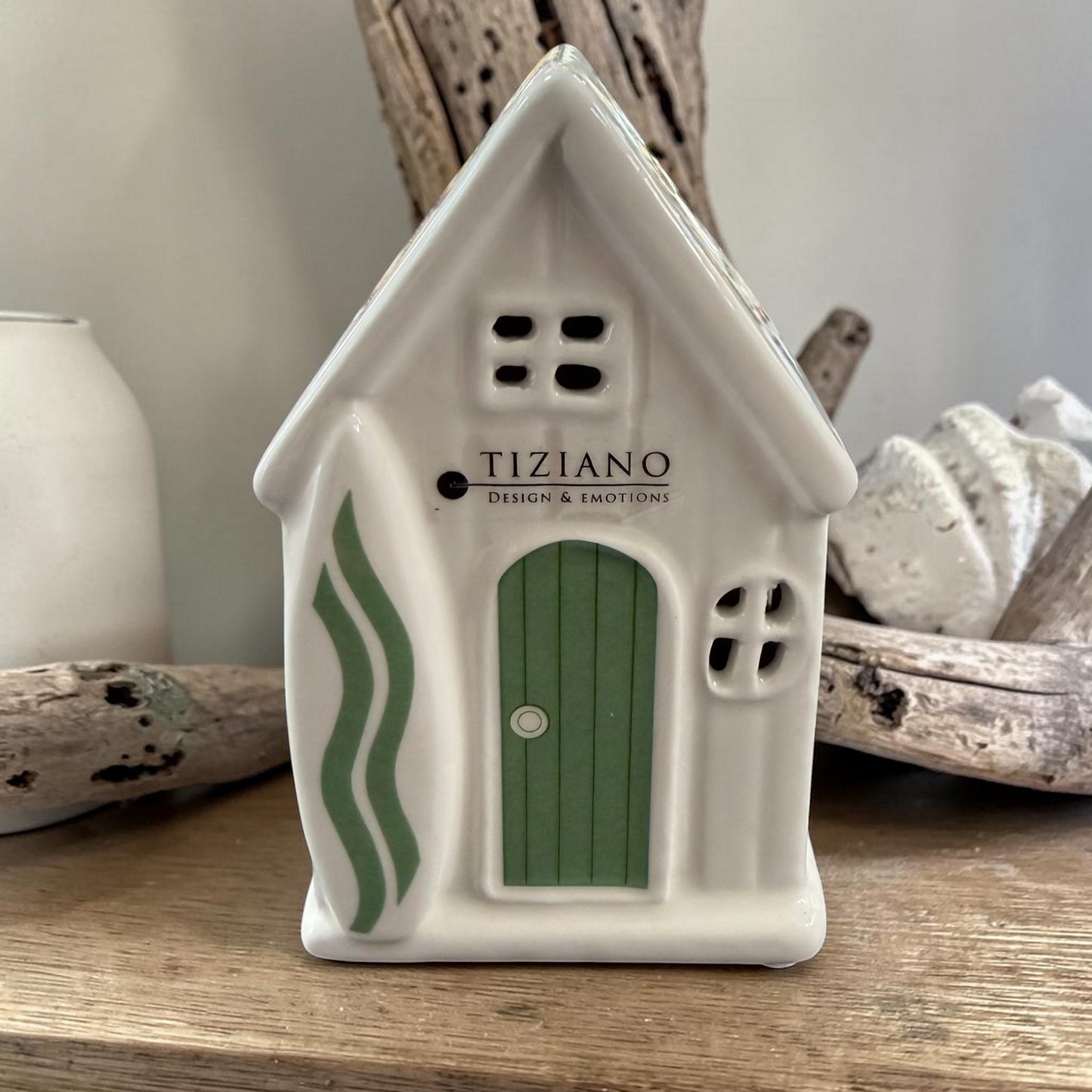 Ein weißes Keramikhaus mit grüner Tür und grünen Seitendetails steht auf einer Holzoberfläche vor dekorativen Holzelementen.