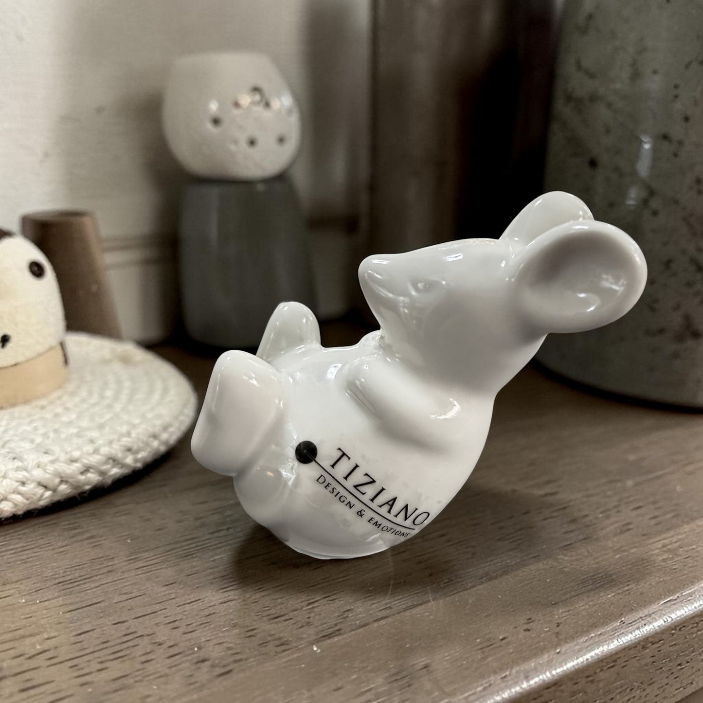Kleine weiße Keramikmaus in liegender Position als dekoratives Wohnaccessoire auf dunklem Holz.