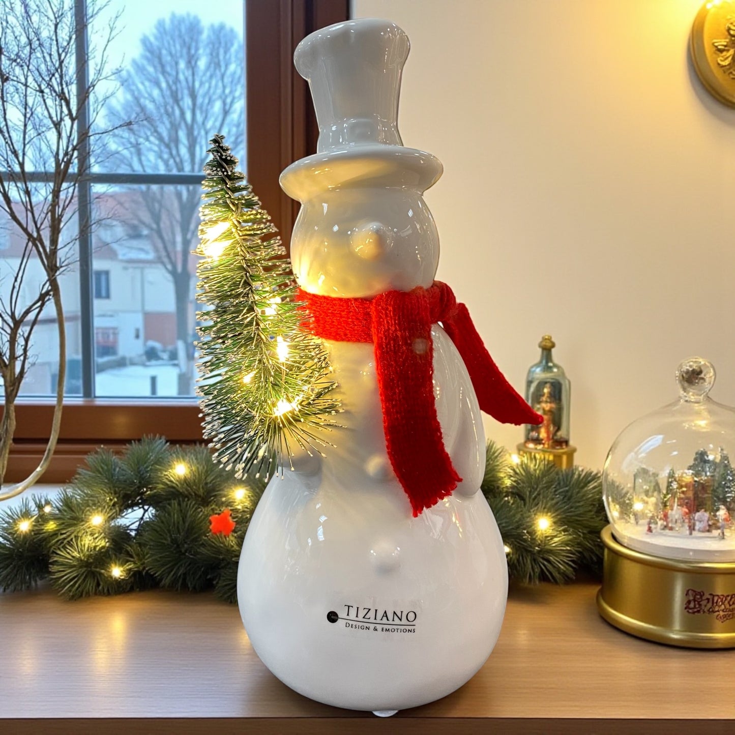 Ein creme-weißer Keramik Schneemann mit rotem Schal und beleuchtetem Tannenbaum, Serie Sören von Tiziano im Ambiente