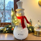 Ein creme-weißer Keramik Schneemann mit rotem Schal und beleuchtetem Tannenbaum, Serie Sören von Tiziano im Ambiente