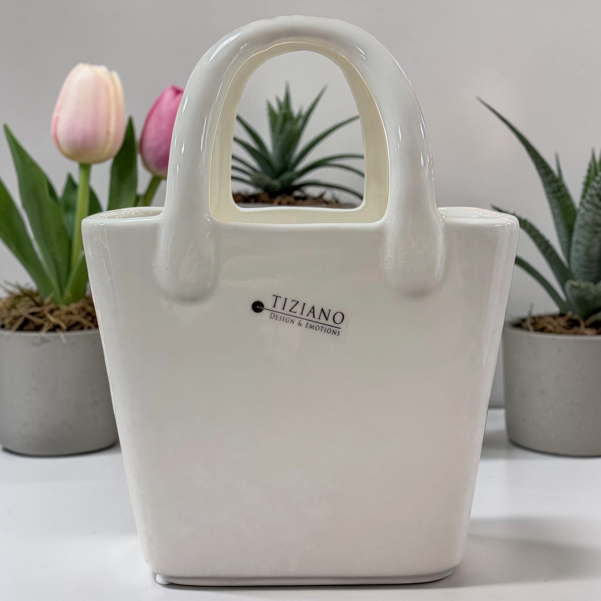 Weiße Keramik-Dekotasche mit Griff von Tiziano, ideal zum Bepflanzen, dekorativ inszeniert vor Pflanzen und Blumen.