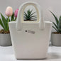 Weiße Keramik-Dekotasche mit Griff von Tiziano, ideal zum Bepflanzen, dekorativ inszeniert vor Pflanzen und Blumen.