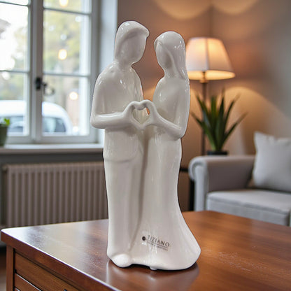 Weiße Keramikfigur eines Paares mit Herzform aus den Händen auf einem Holztisch im Wohnzimmer