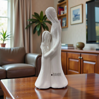 Weiße Keramikfigur mit stilisiertem Mutter-Tochter-Motiv steht auf einem Tisch in einem Wohnraum.