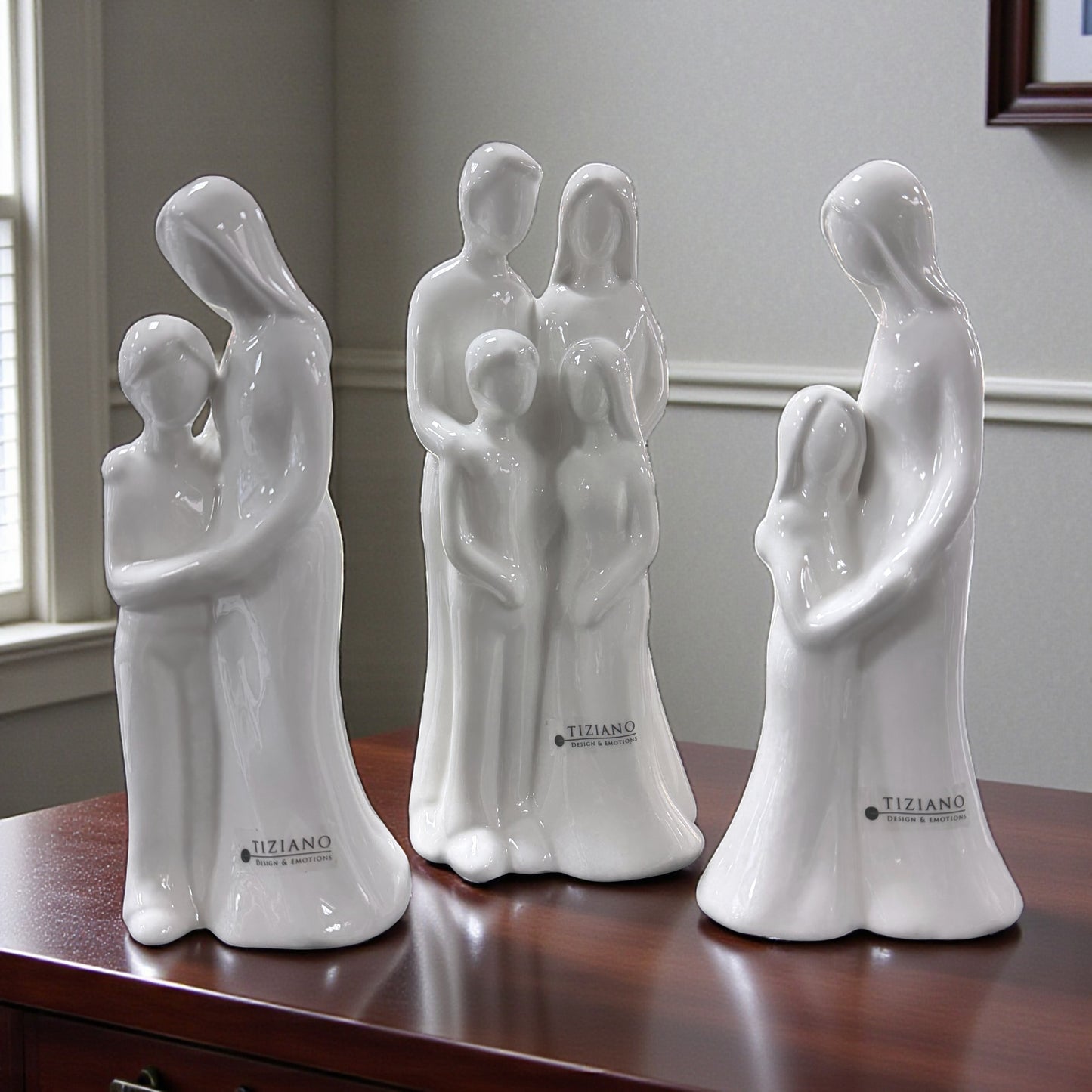 Mehrere weiße Keramikfiguren mit stilisierten Familienmotiven stehen auf einer Holzoberfläche im Innenraum.