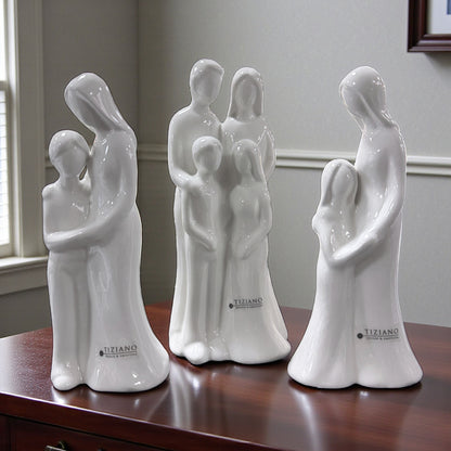 Mehrere weiße Keramikfiguren mit stilisierten Familienmotiven stehen auf einer Holzoberfläche im Innenraum.