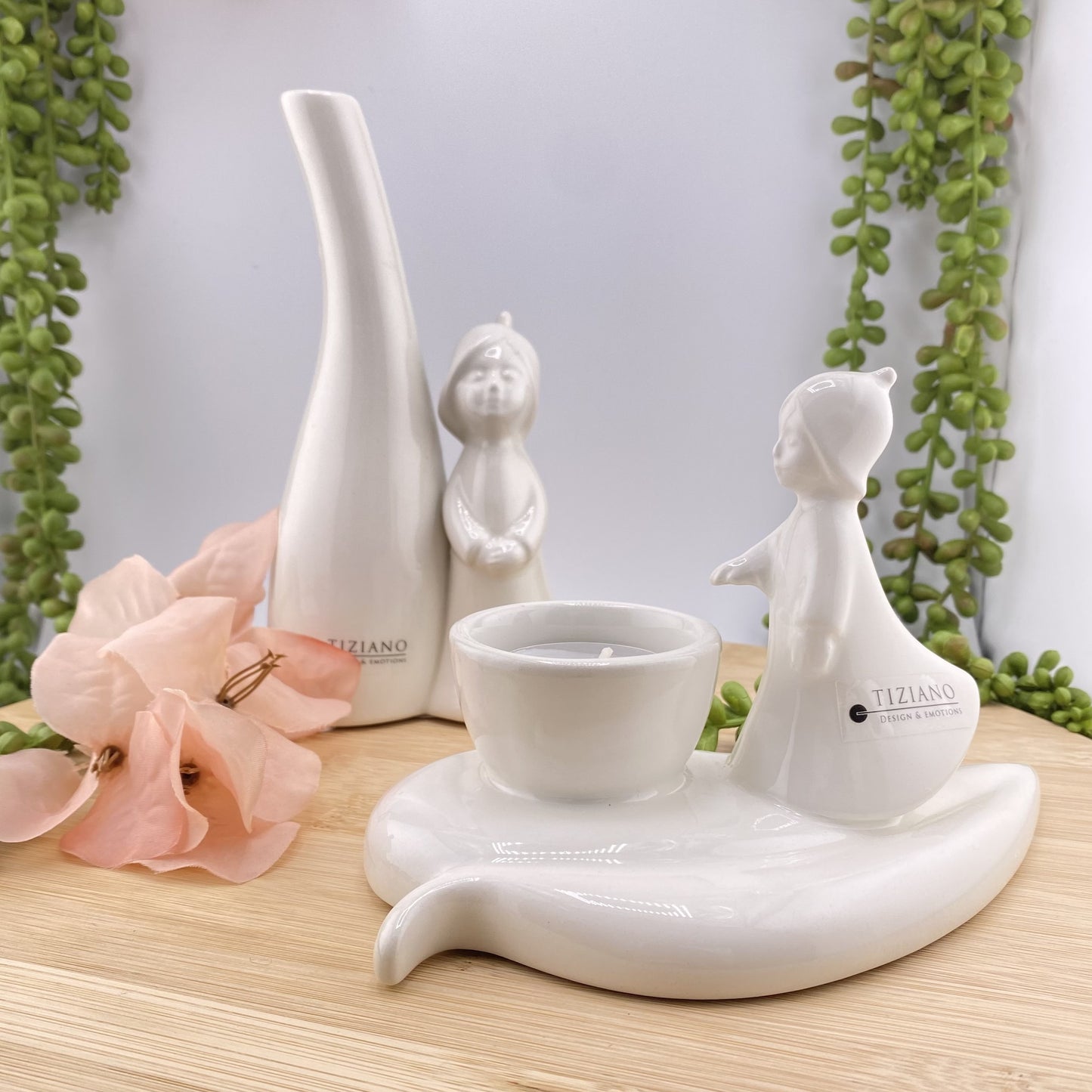 Es sind zwei Dekoobjekte aus creme-weißer Keramik zu sehen. Beide sind mit einer Blumenfee aus Keramik verziert. Eine Dekofigur beinhaltet eine Vase, die andere einen Behälter für ein Teelicht, welches erleuchtet werden kann.