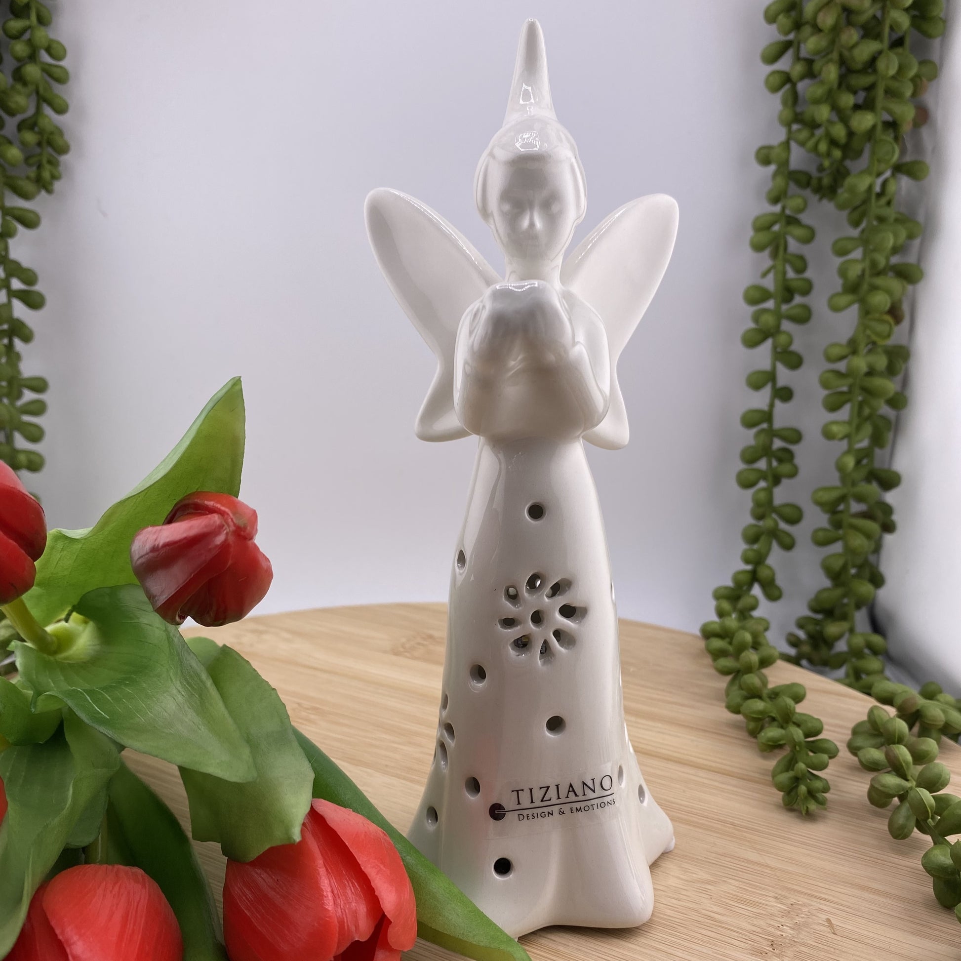 Eine Deko Keramik Fee aus creme-weißer Keramik. Auf ihrem Kleid sind blumenförmigen Aussparungen. In ihren Händen hält die Blumenfee ein Herz und ihre Flügel sind gespreizt. Im Ambiente platziert und 20cm groß.
