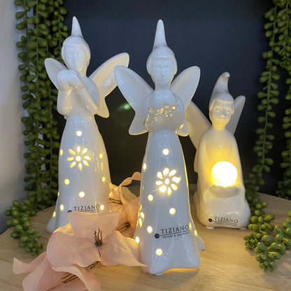 Die Deko Keramik Feen Serie aus creme-weißer Keramik mit LED Beleuchtung in Kombination. Zwei stehende Keramik Feen mit Herz in ihren Händen und blumenförmigen Aussparungen. Eine sitzende Fee mit beleuchteter Kugel in ihren Händen.