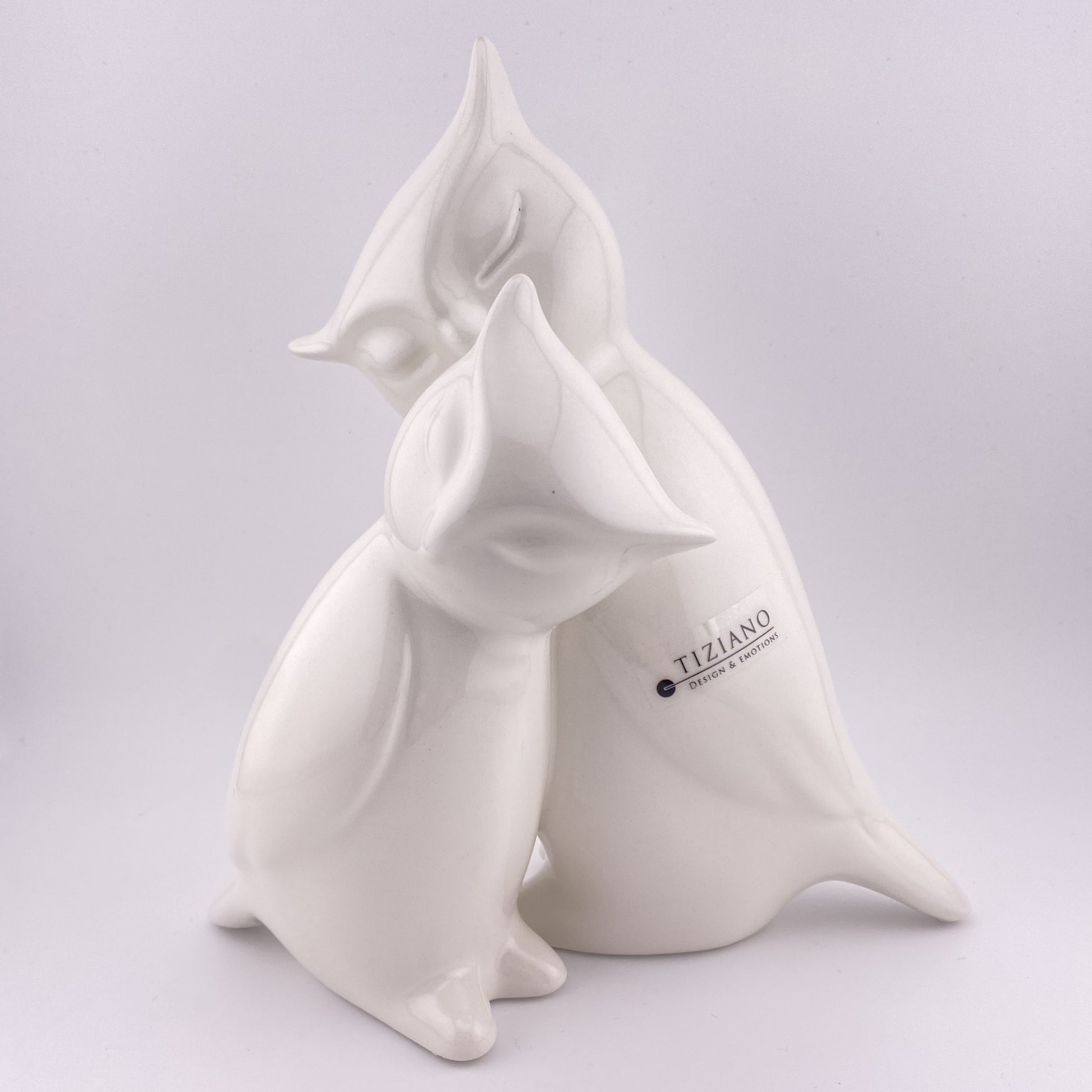 Ein großes Deko Eulenpaar aus creme-weißer Keramik sitzt auf einem Ast und kuschelt miteinander. Das paar ist 20cm und vor weißem Hintergrund platziert. 