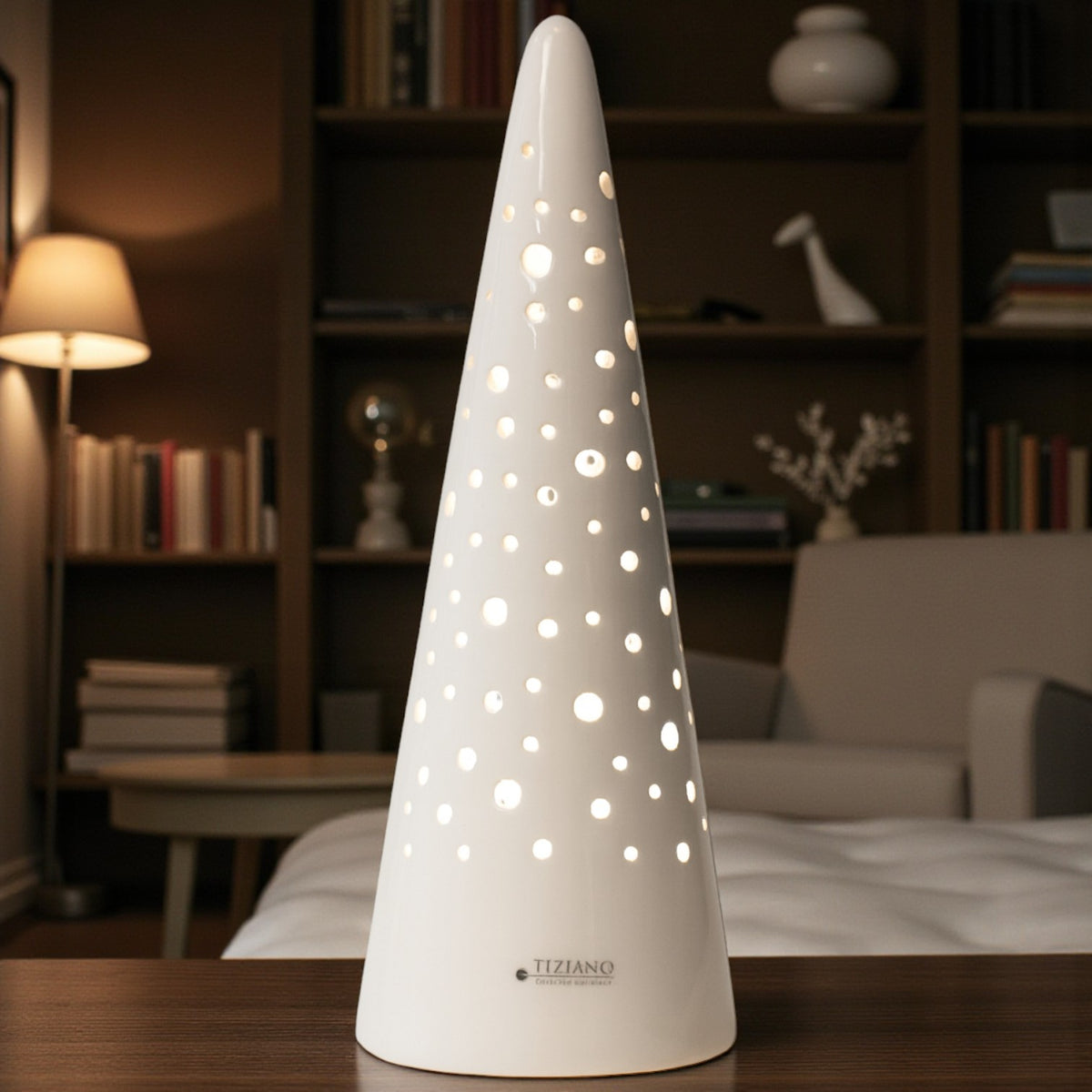 Eine konische, weiße Keramiklampe mit Lochmuster steht auf einem Holztisch in einem Wohnzimmer. Im Hintergrund sind Bücherregale und eine warme Lichtstimmung zu sehen.