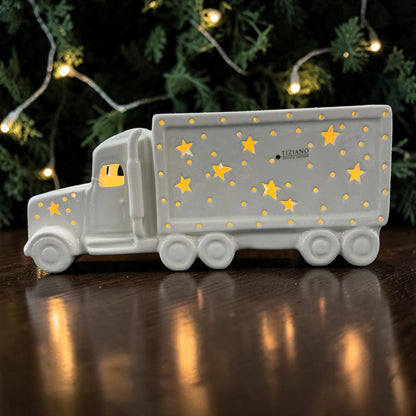 Cremeweißer Tiziano Keramik LED-LKW mit leuchtenden Sternen und Punkten auf einem dunklen Holztisch vor Tannenzweigen und warmweißer Lichterkette.