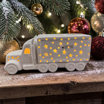 Cremeweißer Tiziano Keramik LED-LKW mit Sternen und warmweißer Beleuchtung vor einem geschmückten Weihnachtsbaum mit Weihnachtskugeln.