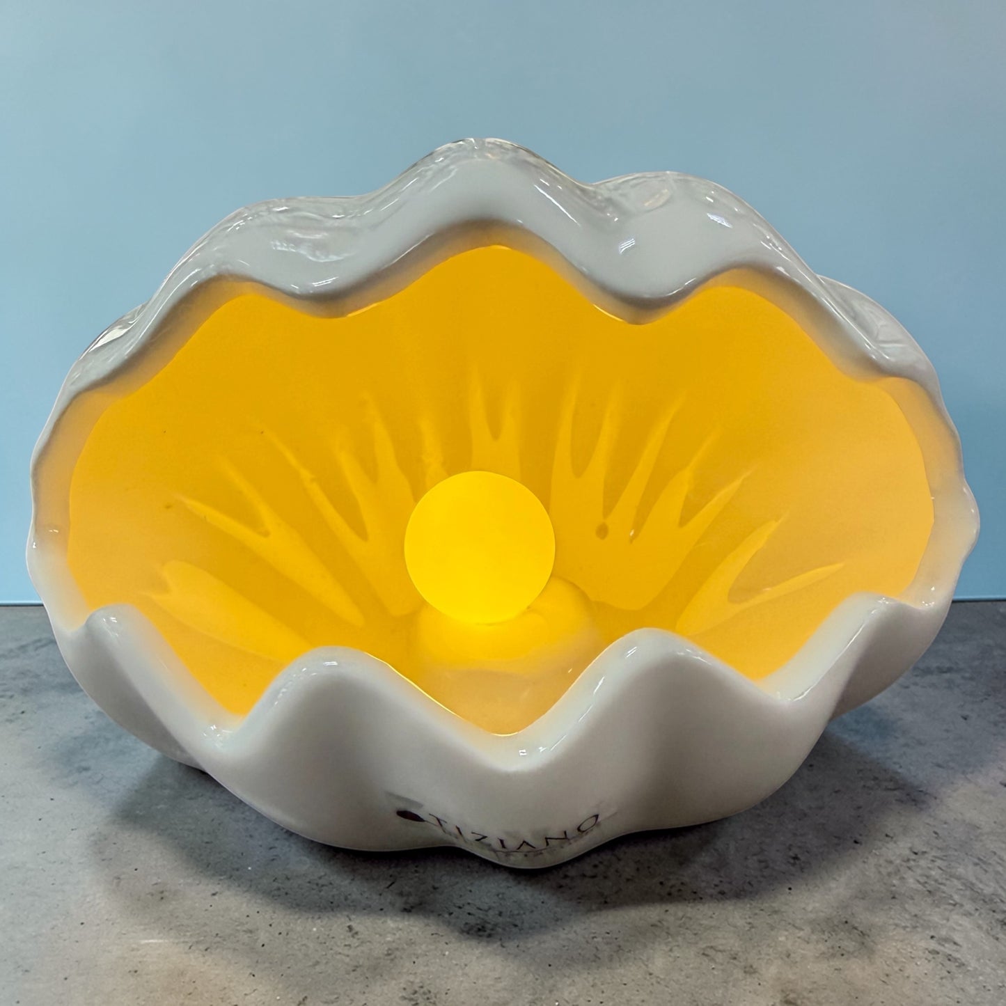 Eine weiße Keramik-Muschel mit integrierter LED-Kugel leuchtet warm und wird einzeln vor neutralem Hintergrund präsentiert.