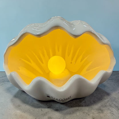 Eine weiße Keramik-Muschel mit integrierter LED-Kugel leuchtet warm und wird einzeln vor neutralem Hintergrund präsentiert.