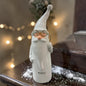 Cremeweißer Tiziano Keramik-Nikolaus mit langer Mütze, Bart und goldfarbener Brille vor warmweißer Lichterkette und weißer Schneedekoration.
