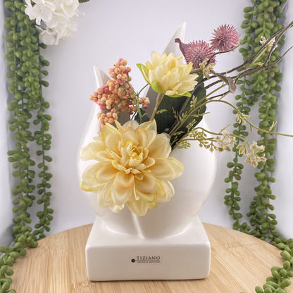 Eine große Pflanzenschale aus creme-weißer Keramik, die mit Trockenblumen im Ambiente platziert ist. Die Vase besteht aus einem Sockel, auf dem zwei Blätter eine tulpenartige Vase und damit eine Öffnung formen. Die Keramikvase ist 26cm groß. 