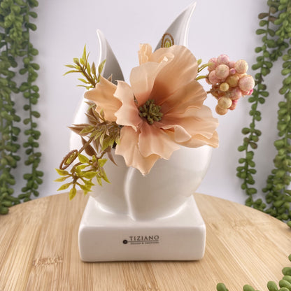 Eine Pflanzenschale aus creme-weißer Keramik, die mit Trockenblumen im Ambiente platziert ist. Die Vase besteht aus einem Sockel, auf dem zwei Blätter eine tulpenartige Vase und damit eine Öffnung formen. Die Keramikvase ist 20cm groß. 