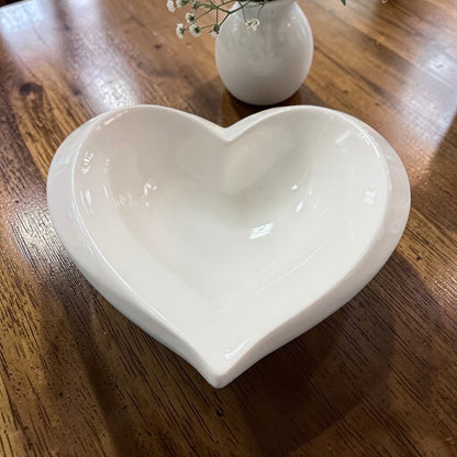 Herzförmige Keramikschale in Creme auf Holztisch mit Vase im Hintergrund