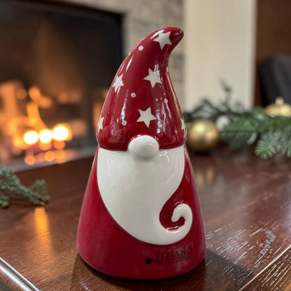 Roter Tiziano Keramik Weihnachtsmann mit weißem Bart und Sternenmütze auf einem Holztisch vor einem Kamin.