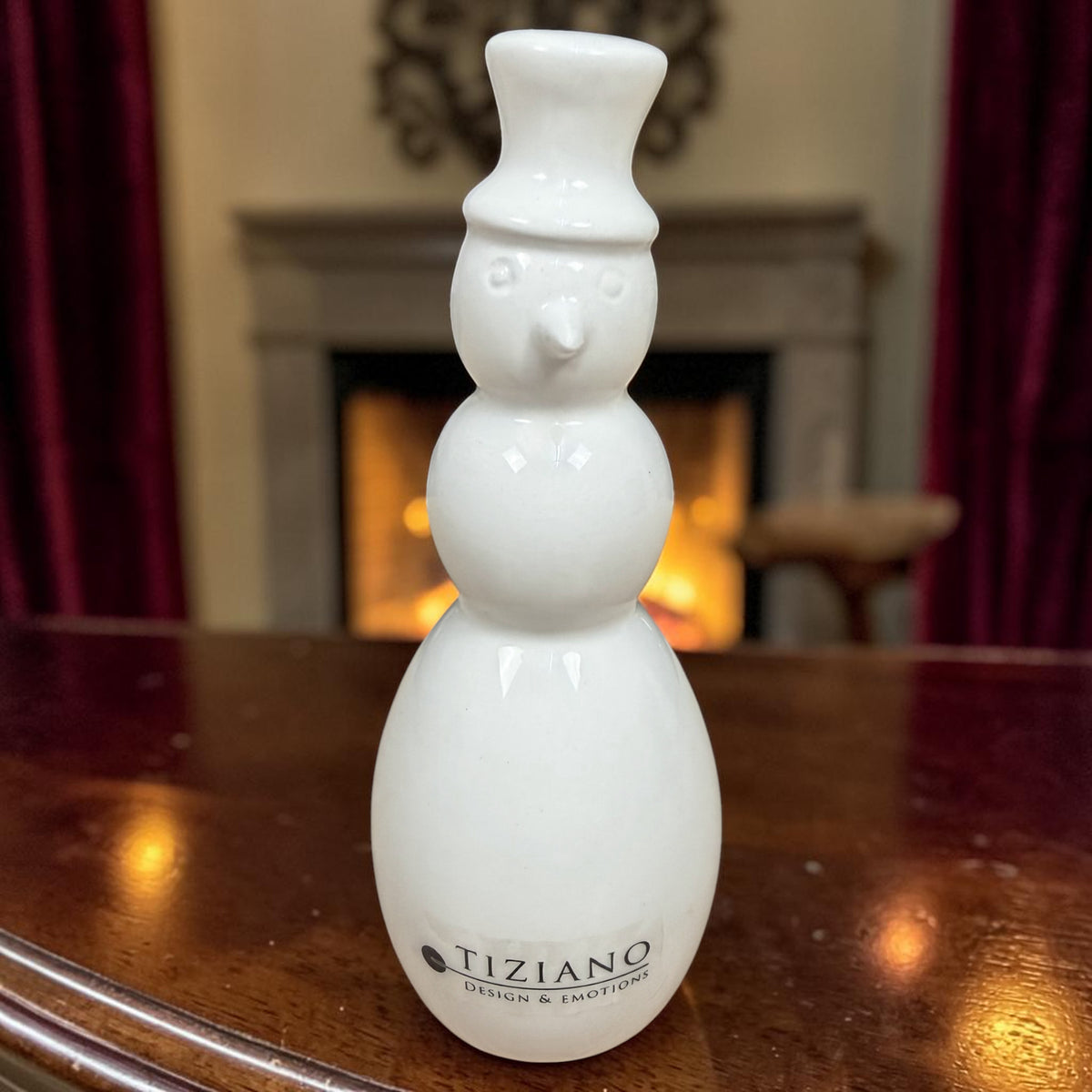 Hoher cremeweißer Tiziano Keramik-Schneemann mit Zylinder vor einem Kamin und weihnachtlicher Beleuchtung.