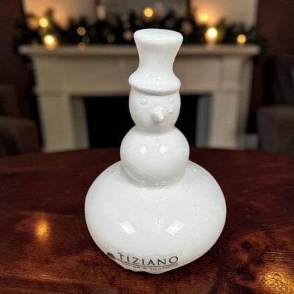 Kleiner cremeweißer Tiziano Keramik-Schneemann mit Zylinder auf einem Holztisch vor weihnachtlich beleuchtetem Kamin.