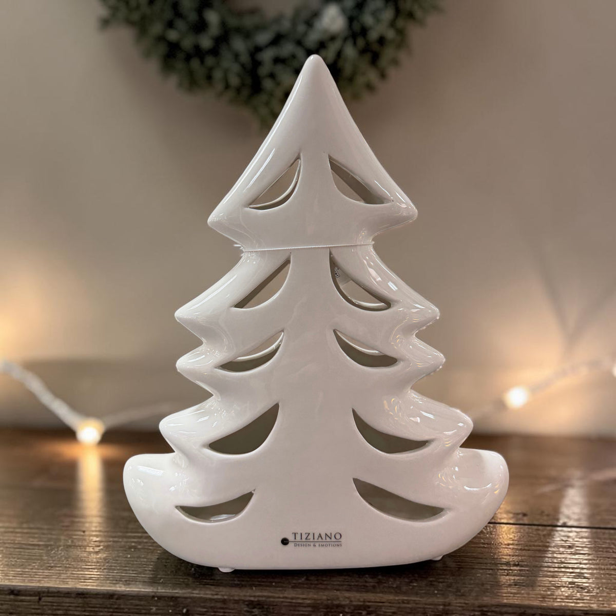 Cremeweißer Tiziano Keramik Tannenbaum mit geschwungenen Durchbrüchen auf einem Holztisch vor dezentem Hintergrund.