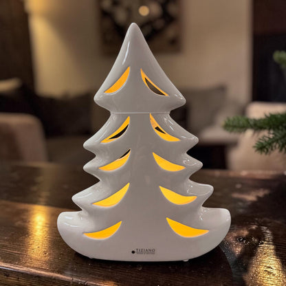 Cremeweißer Tiziano Keramik Tannenbaum mit warm beleuchteten geschwungenen Durchbrüchen auf einem dunklen Holztisch.