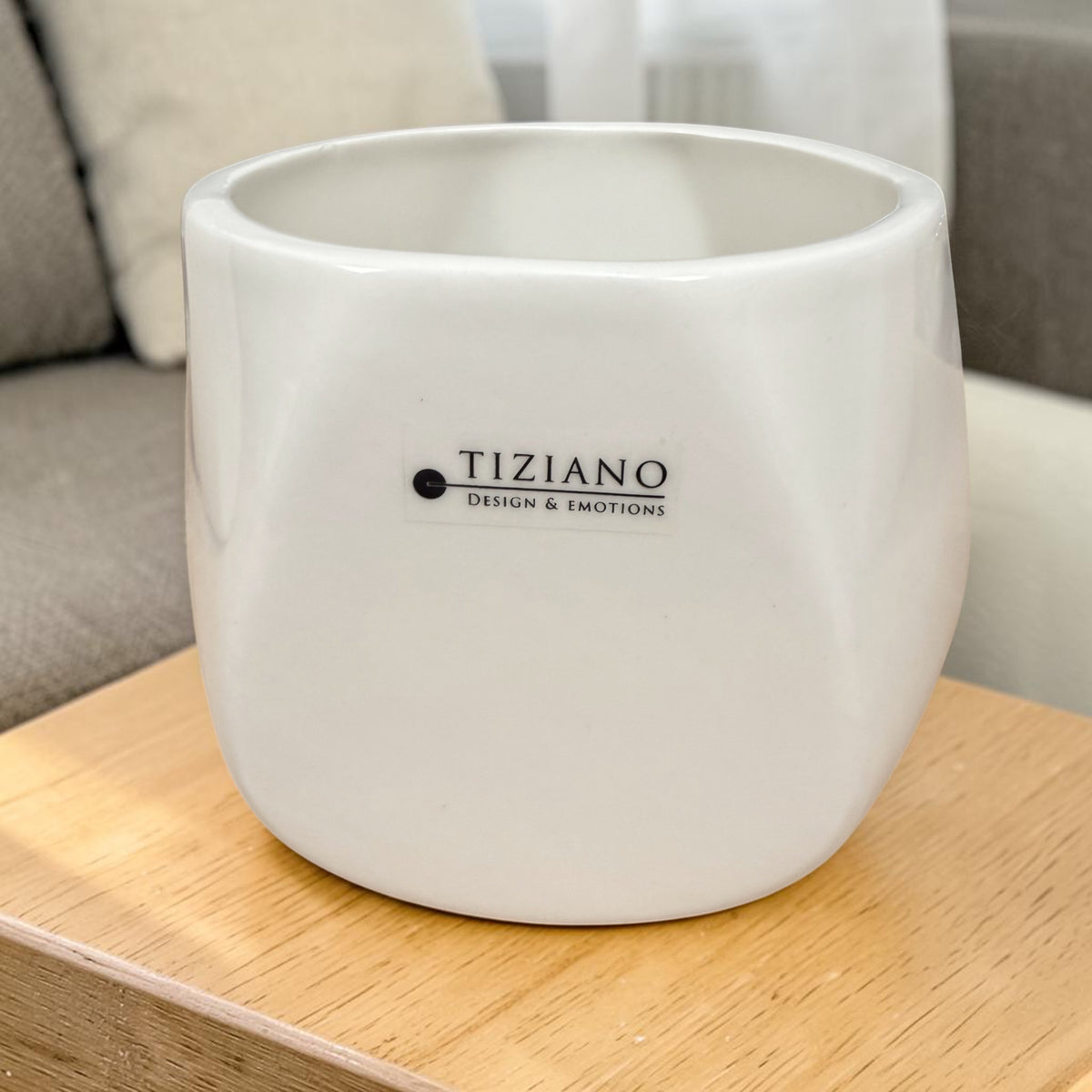Runder cremeweißer Tiziano Keramikübertopf mit leicht facettierter Form auf einem hellen Holztisch.