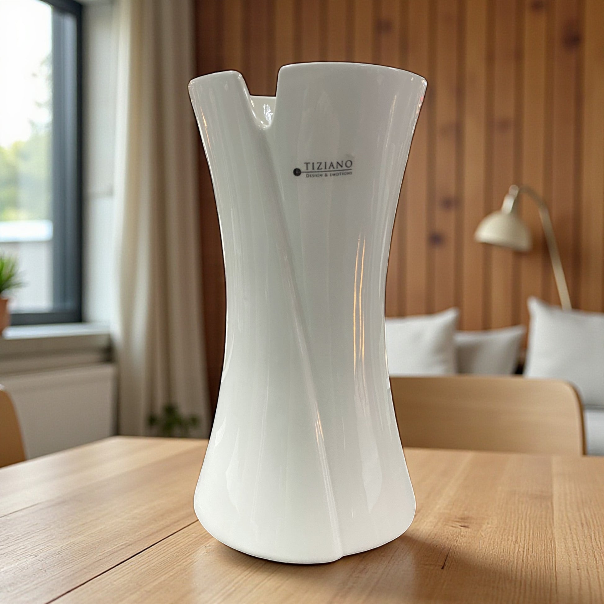 Weiße Keramikvase von Tiziano mit geschwungener, organischer Form und leicht nach außen geöffnetem Rand, auf Holztisch in Wohnraum platziert